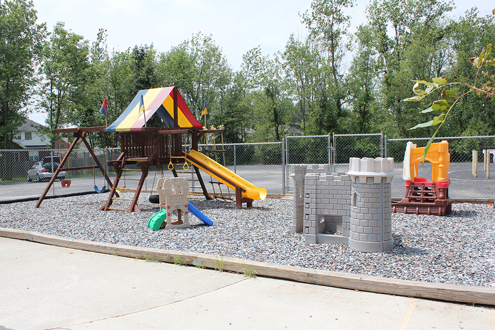 An outdoor playground with a slide, swings, and plastic play structures on gravel.