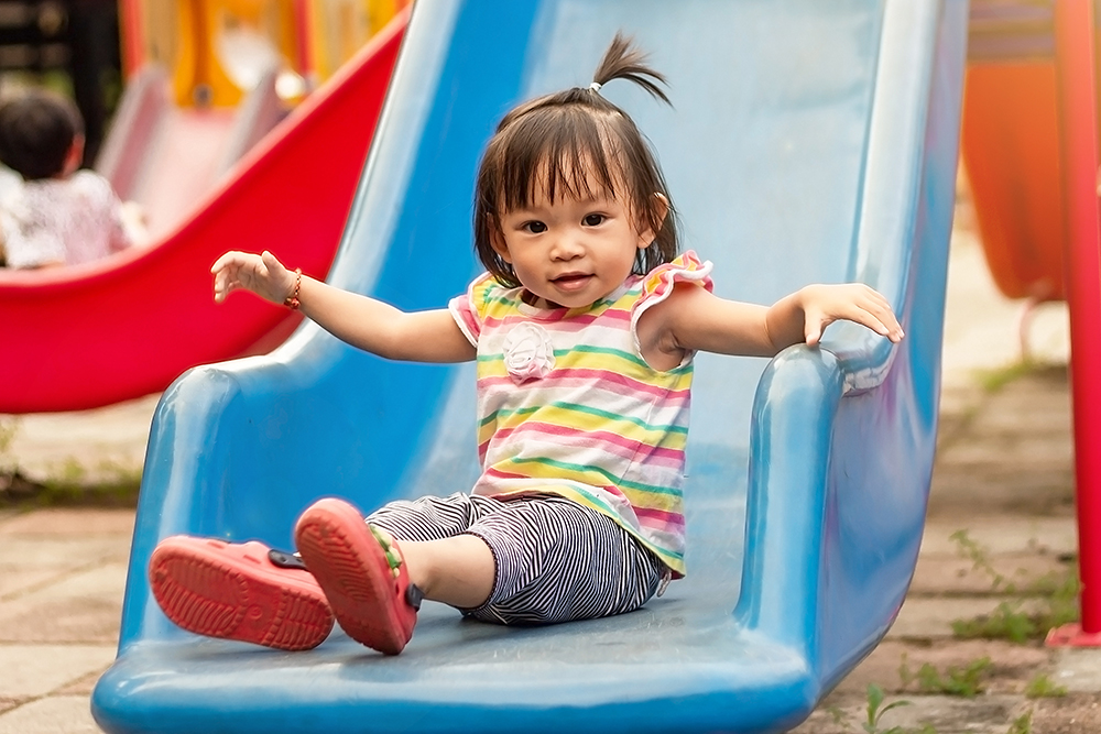 A little girl slides down a blue playground slide while smiling.