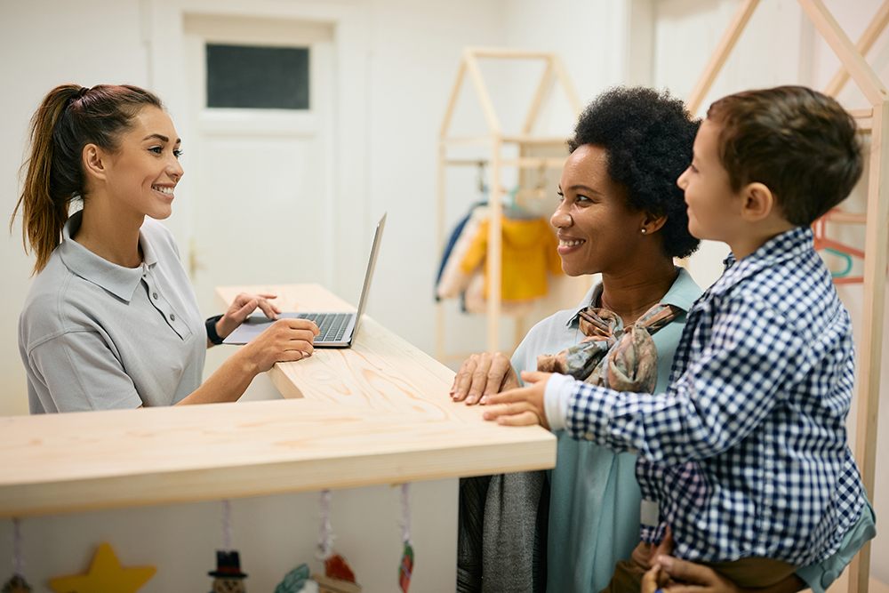 A receptionist greeting a parent and child at a childcare center.