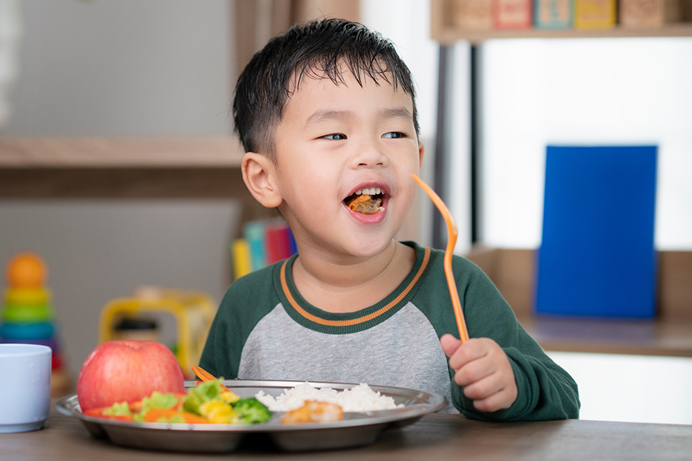 A child eating from a plate of food with vegetables, rice, and fruit.