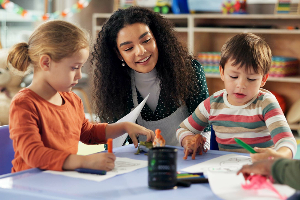 A teacher helping two young children with coloring.