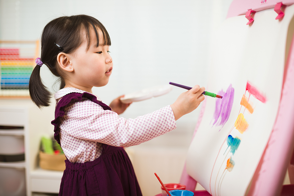 A young girl with pigtails painting colorful strokes on an easel.
