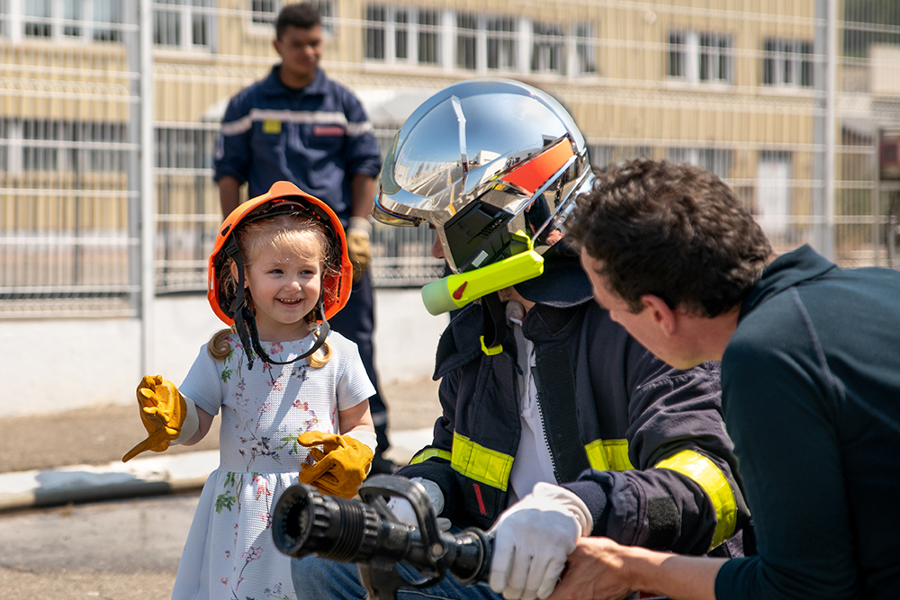 Child wearing a firefighter helmet while talking to firefighters.