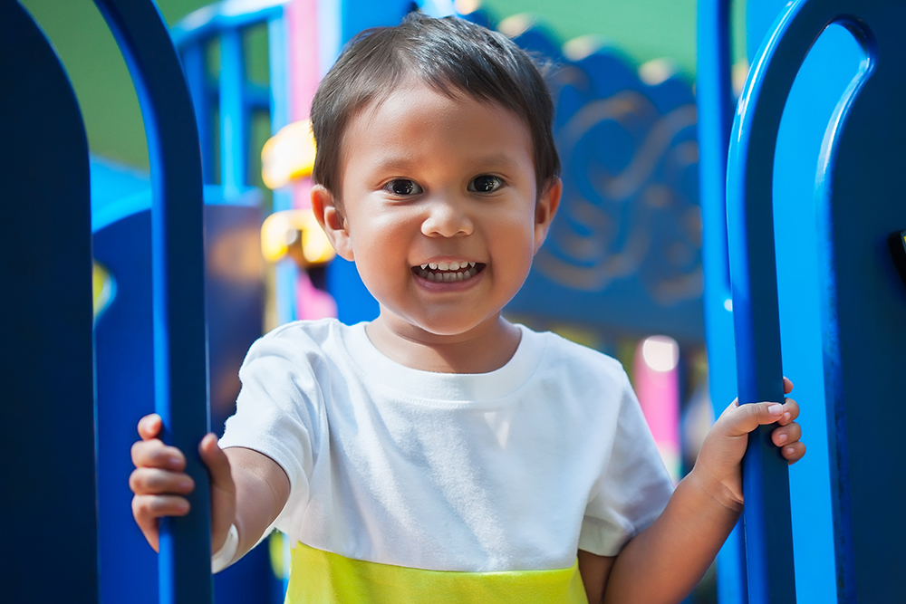 A young boy smiling while holding onto playground equipment.